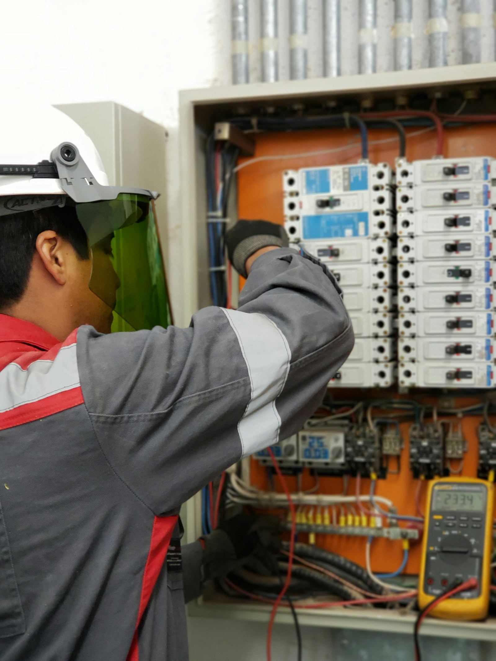 A technician in a hard hat testing an electrical panel